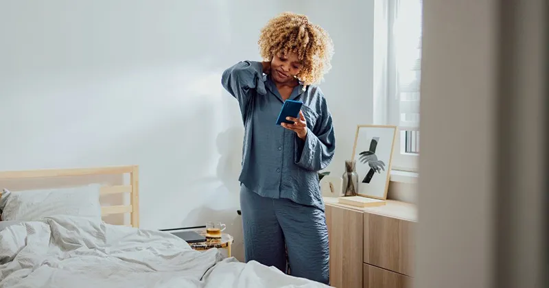 woman in bedroom holding her stiff neck in pain