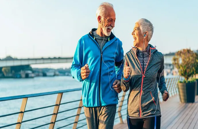 senior citizen women and man smile at each other on boardwalk near water