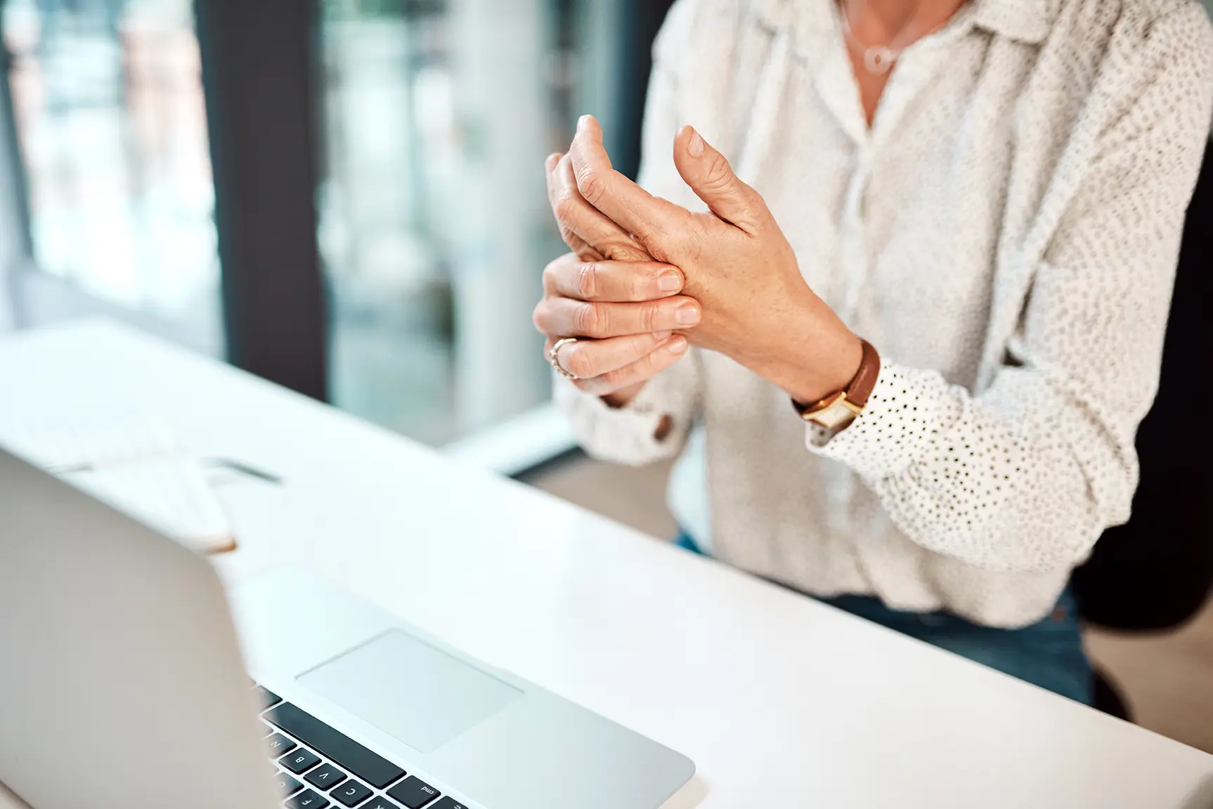 Woman at a laptop rubbing her wrist and hand due to pain from Thoracic Outlet Syndrome or Carpal Tunnel Syndrome